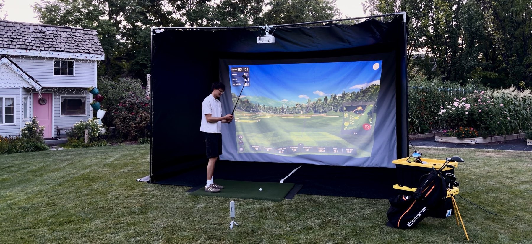 The full TILT golf simulator set up on a lawn, with the enclosure, screen, hitting mat and equipment
